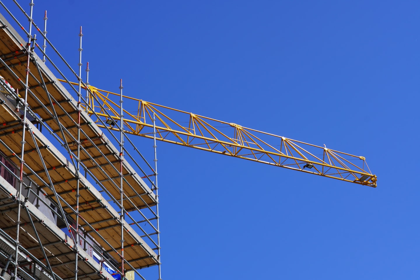 Metal scaffolding stands beside a yellow crane at a construction site.