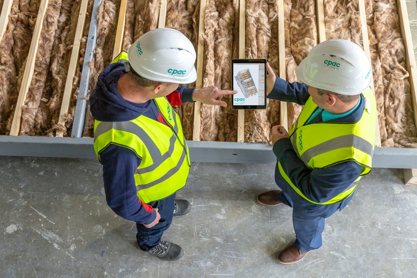 Two construction workers discuss a digital tablet at a job site.