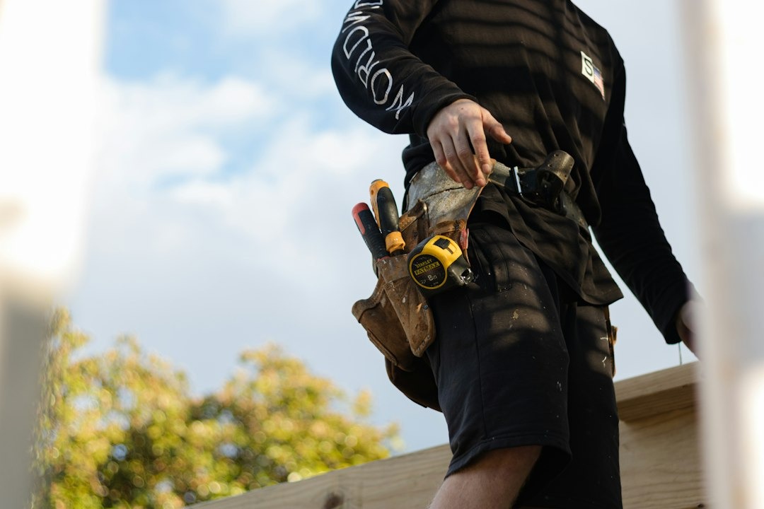 Carpenter on wooden beams with tools in belt.
