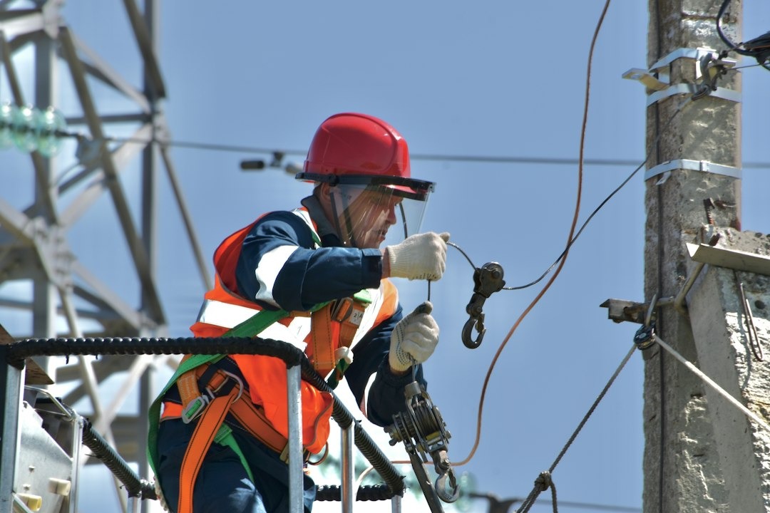 Worker in a lift repairs electrical equipment under blue sky.